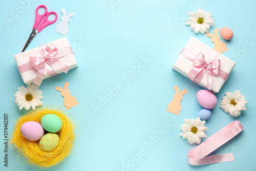 Frame made of gifts, Easter eggs, paper rabbits and flowers on blue background