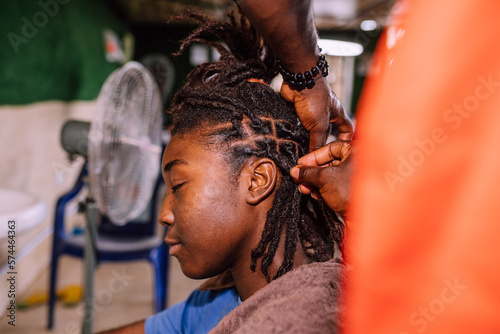 A young queer masculine woman retwisting her dreadlocks