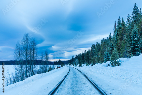 Lenticular clouds and rail tracks in snow with pines and bare trees - Lassen County California, USA.