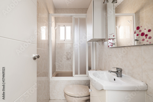 Bathroom with shower with sliding door screen  cream-colored tiles on walls and floors and bathroom cabinet with white porcelain sink with mirror