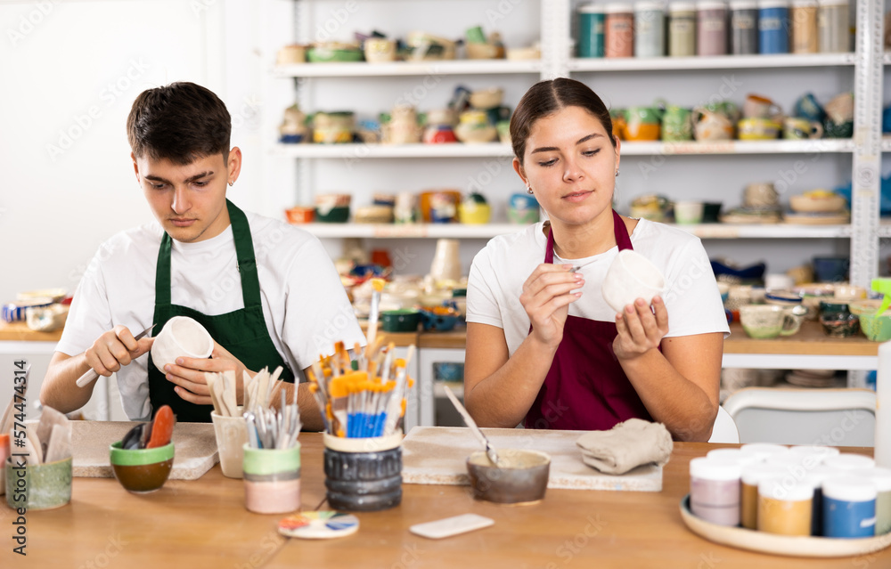 Young woman and young man making clay ceramic cups in workshop