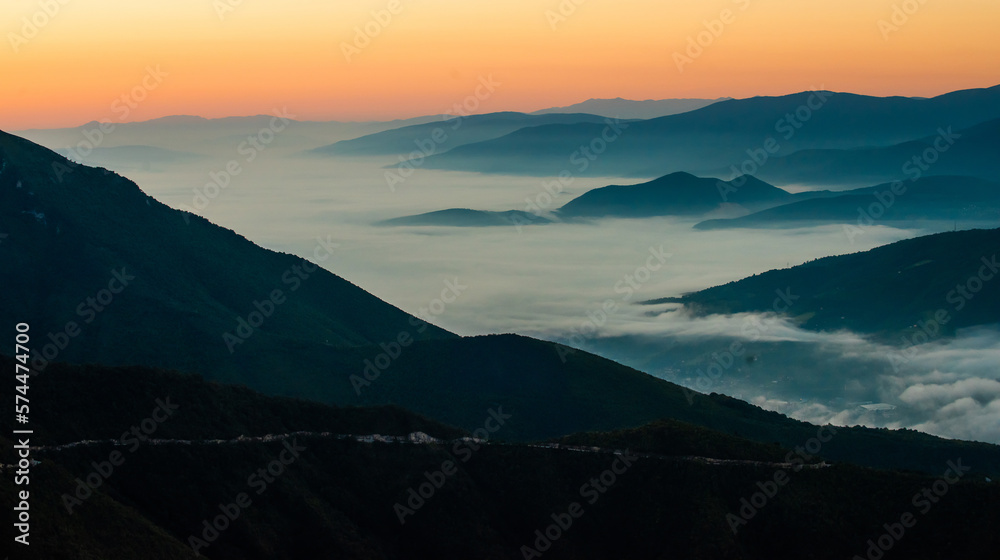 Obraz premium Mountain range with visible silhouettes through the morning colorful fog