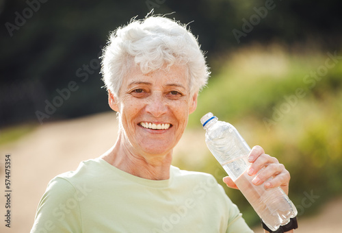 Elderly woman with short grey hair drinking water after exercising, portrait in the park