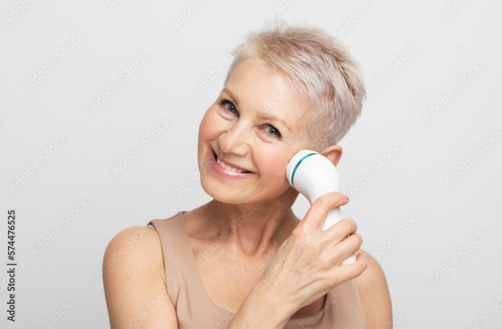 Naklejka premium Beautiful 60s woman holding a massager in her hand and use on face. Spa technique skincare ads.