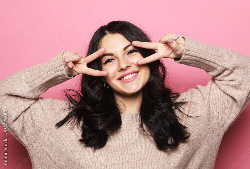 Young brunette woman smiling and show v-sign over pink background Young brunette woman smiling and show v-sign over pink background