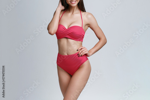 The body of a slender young girl in a fashionable swimsuit on a studio gray background. Diet, fitness, healthy lifestyle