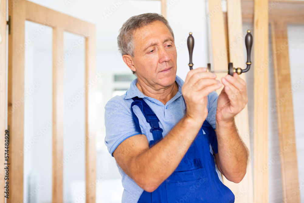 Fototapeta premium Serious middle-aged male locksmith examining a doorknob before installing it on a door in a house