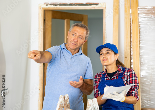 Casual middle-aged man discussing the future construction site with the female repairer in uniform in the house