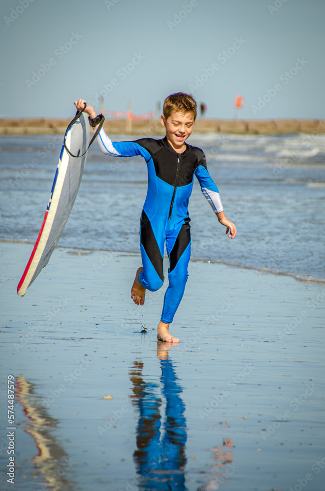 Young Preteen Boy Wearing Rash Suit Running on the Beach with A Boogie