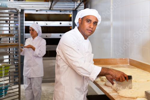 Portrait of confident latin american bakery owner engaged in breadmaking, preparing portioned pieces of dough for baking