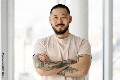 Valokuva Portrait of handsome smiling Asian man with arms crossed and stylish tattoos loo
