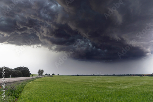 Storm forming dark clouds over green grass field.