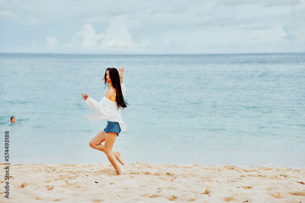 A woman runs along the beach in summer clothes on the sand in a yellow T-shirt and denim shorts white shirt flying hair ocean view A woman runs along the beach in summer clothes on the sand in a yellow T-shirt and denim shorts white shirt flying hair ocean view