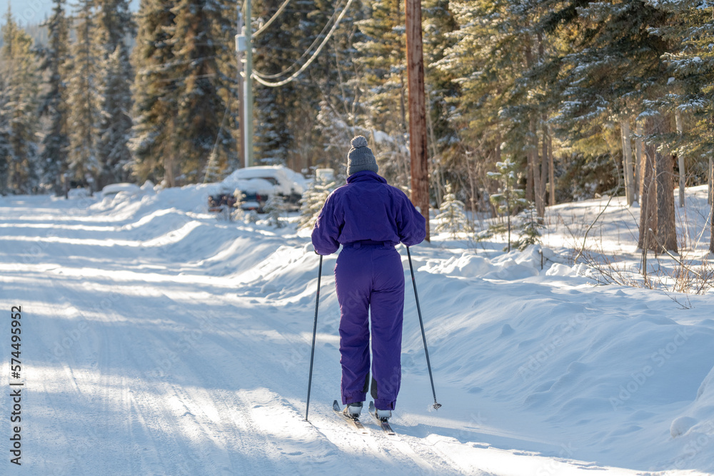 Woman in purple one piece ski suit with cross country skis in winter season. Boreal forest background and snow covered ground. 