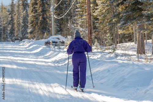 Woman in purple one piece ski suit with cross country skis in winter season. Boreal forest background and snow covered ground. 
