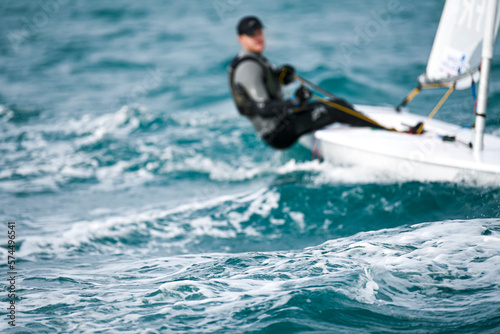 A close-up of a wave at sea with a unrecognizable person sailing in the background