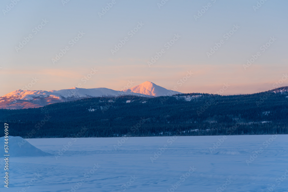 Winter landscape scenery in Yukon Territory at sunrise with pink pastel tones on distant mountains. 