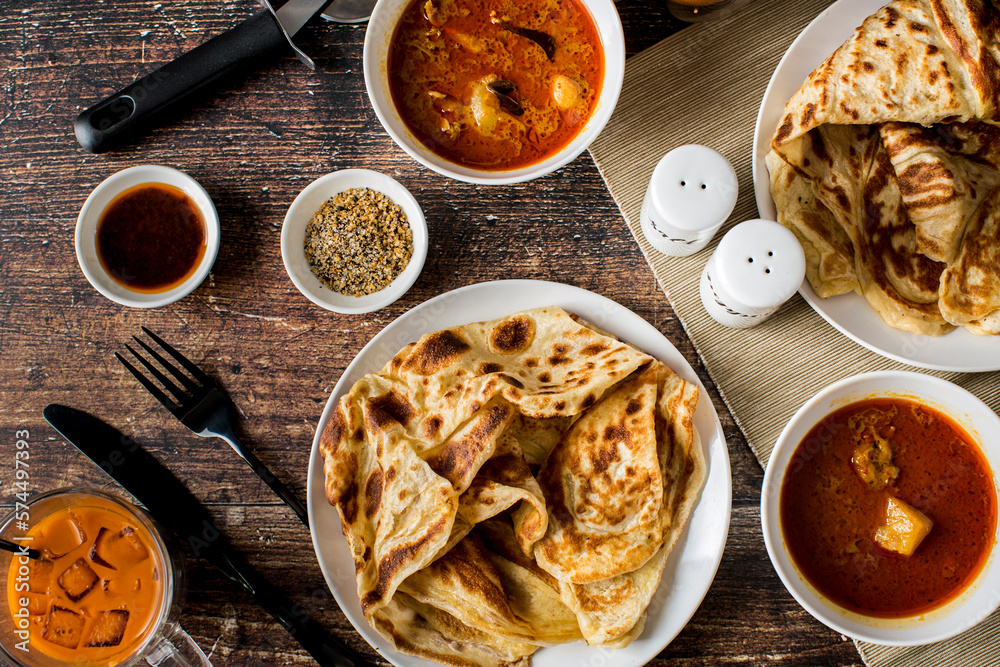 Malaysian Cuisine Roti Canai - Crispy Indian style pancake served with curry chicken dipping sauce with Thai ice tea on wooden table. Malaysian Cuisine Roti Canai - Crispy Indian style pancake served with curry chicken dipping sauce with Thai ice tea on wooden table.