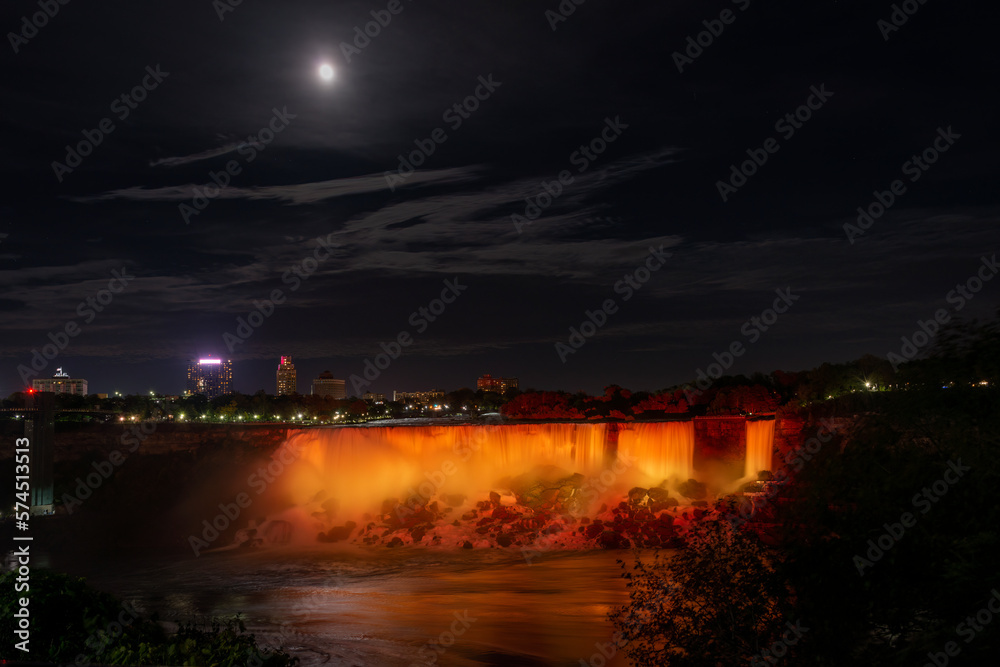 Niagara Falls lit up in gold and yellow under the moonlight. Ontario, Canada.