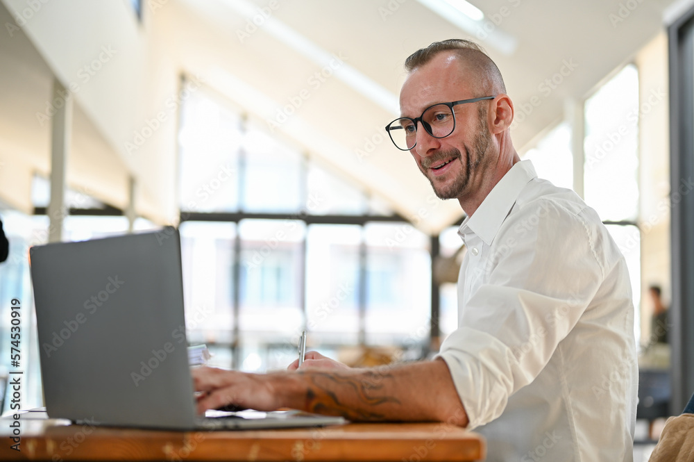 Side view of a smart Caucasian businessman using laptop, managing his financial tasks Side view of a smart Caucasian businessman using laptop, managing his financial tasks