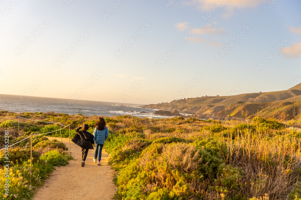 Kids walking on a hiking path at sunset towards ocean on the central California coast
