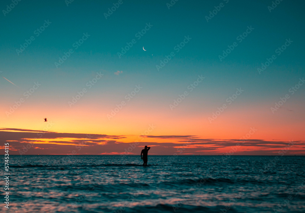 silhouette of a man in the ocean during sunset with moon in the background