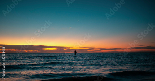 silhouette of a man in the ocean during sunset with moon in the background