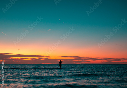 silhouette of a man in the ocean during sunset with moon in the background photo