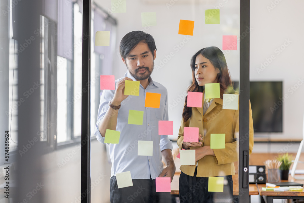 Team of Business female employee with many conflicting priorities arranging sticky notes commenting and brainstorming on work priorities colleague in a modern office.
