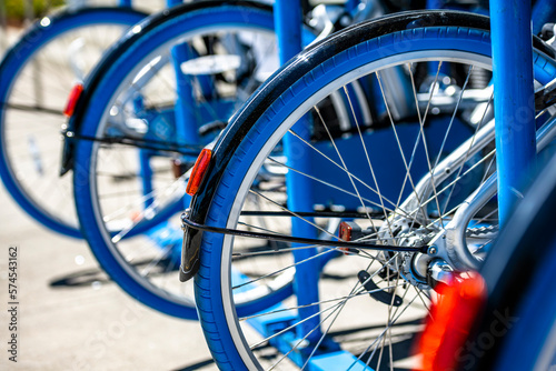 Bright blue bicycles ready for rent and public use stand in a row in a bicycle parking lot on a city street