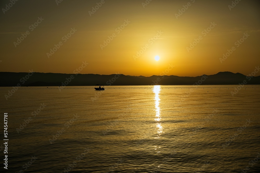Sunset at the sea on a chain of hills, the entire sky shines in golden yellow colors, the sun is reflected in the water, on the sea a small boat. Sunset at the sea on a chain of hills, the entire sky shines in golden yellow colors, the sun is reflected in the water, on the sea a small boat.