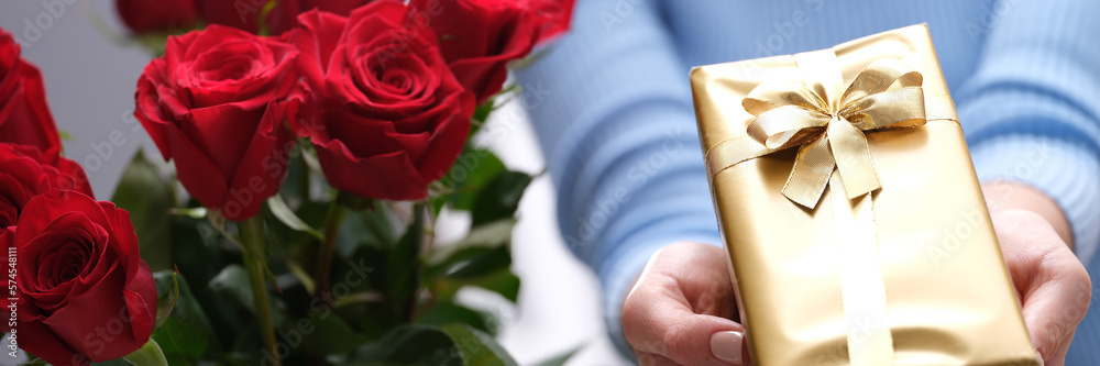 Bouquet of red roses and golden gift box in hands of courier