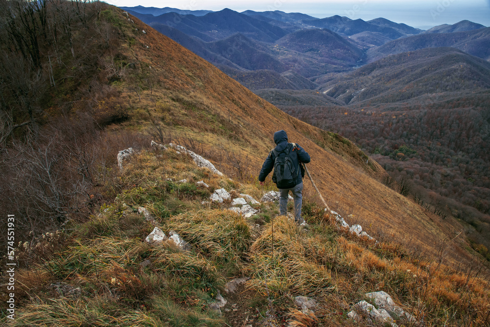 A young man on top of a mountain enjoying nature. A young man with a backpack descends from the top of the mountain. A tourist in the mountains. A man going hiking in the Caucasus mountains.