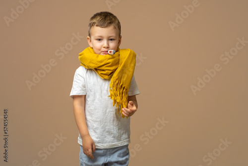 Beautiful kid boy wearing casual t-shirt and yellow scarf standing over isolated light background with thermometer in mouth. Concept of illness and fever, flu and cold, virus sick.