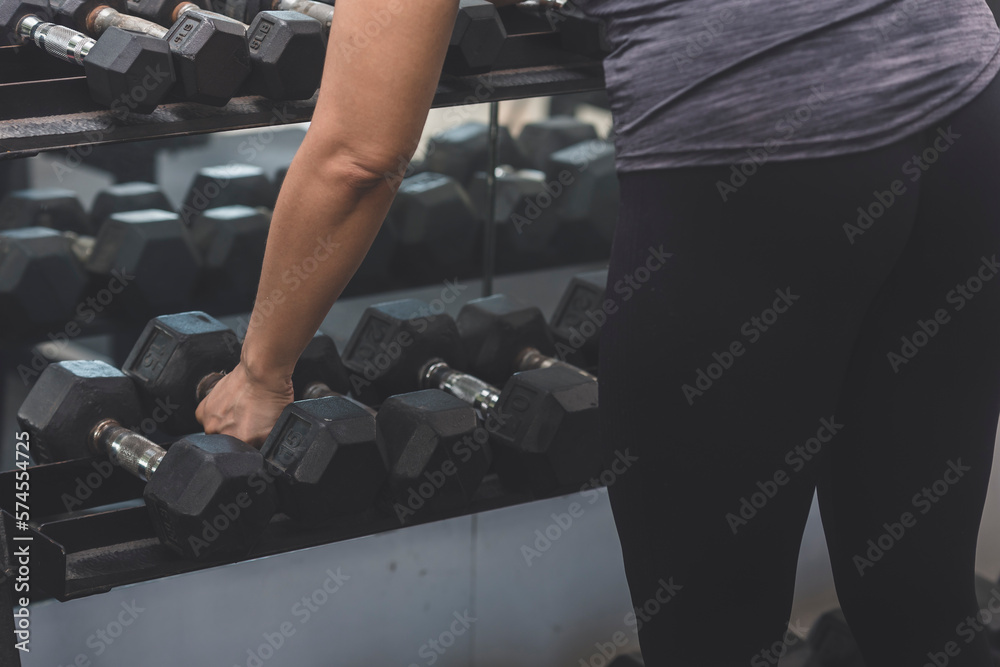 An anonymous woman picking up dumbbells from the rack barehanded. An anonymous woman picking up dumbbells from the rack barehanded.