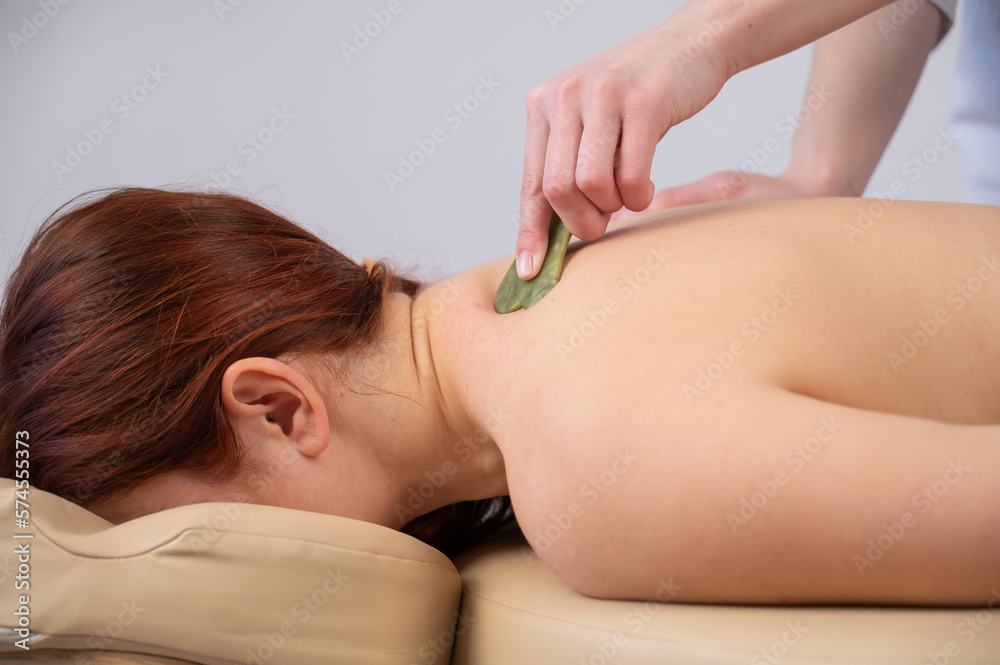 The masseur makes a back massage with a gouache scraper to a female client. The masseur makes a back massage with a gouache scraper to a female client.