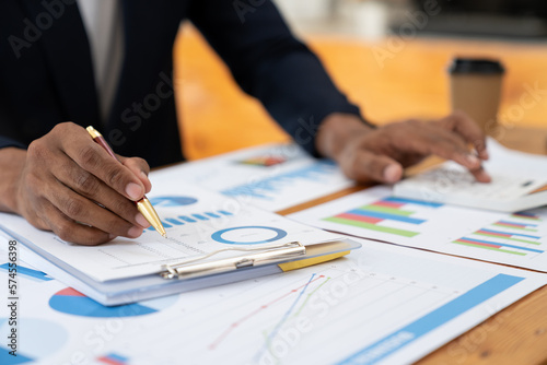 Young asian businessman pointing to data graph analyzing financial reporting situation with a calculator to calculate investment and accounting sitting at the table showing business growth.