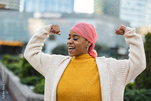 Photo Latina woman, fighting breast cancer, wears a pink scarf, and clenches her arms