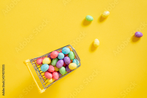  Happy easter.Shopping cart with colorful glitter easter eggs on the yellow background.Top view