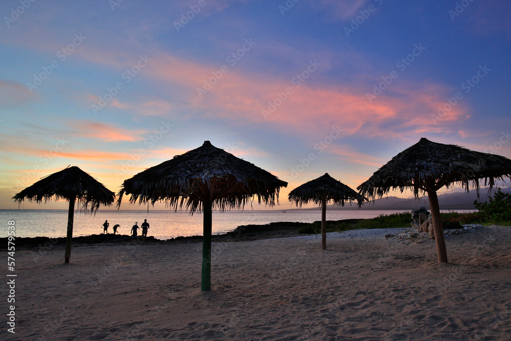 Palm branch umbrellas silhouetted at sunset on beach near Playa Ancon, Trinidad, Cuba Palm branch umbrellas silhouetted at sunset on beach near Playa Ancon, Trinidad, Cuba