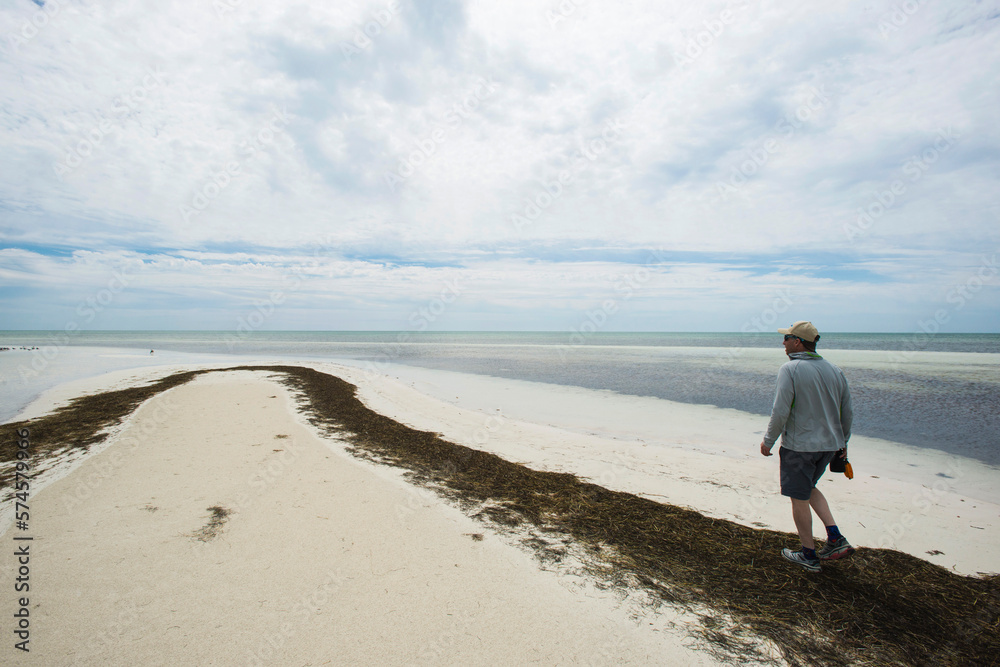 Fisherman Walking Along The Weed Covered Beach In The Florida Keys