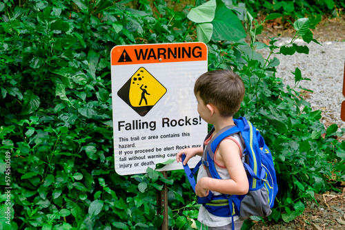 Young boy standing by warning sign on hiking trail photo