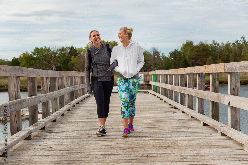Two women walk on a dock laughing Two women walk on a dock laughing