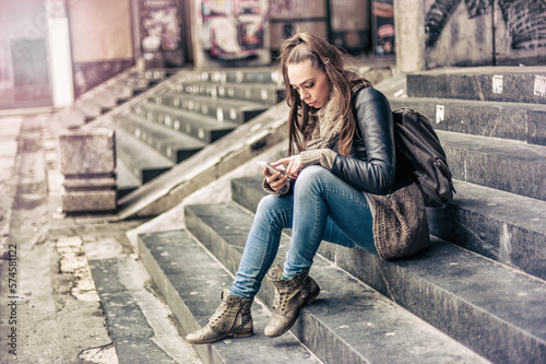 Long hair brunette woman sitting on city stairs and using mobile phone in downtown. Toned