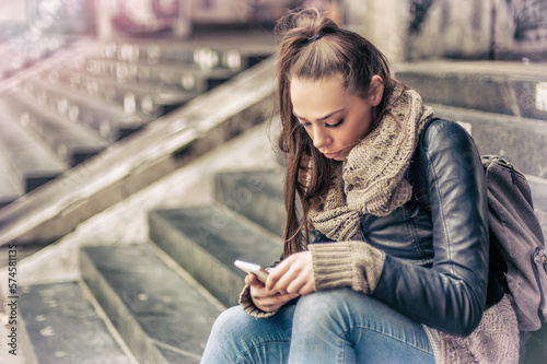 Long hair brunette woman sitting on city stairs and using mobile phone in downtown. Toned