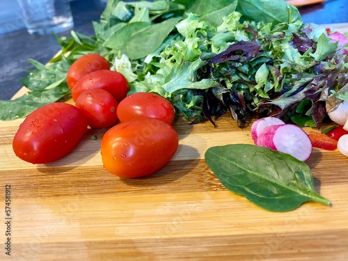 Salad greens tomatoes basil onions raddish on cutting board