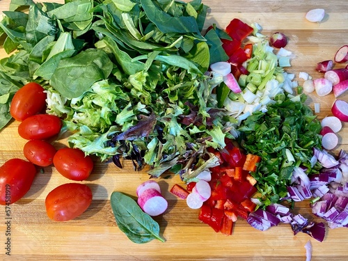 Salad greens tomatoes basil onions raddish on cutting board