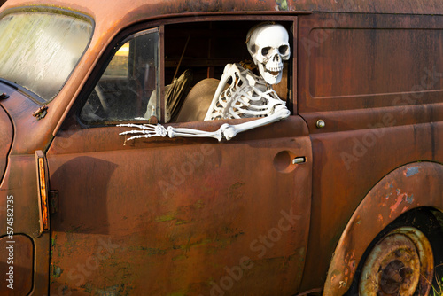 Human skeleton sitting in a rusty old car and looking out of the window