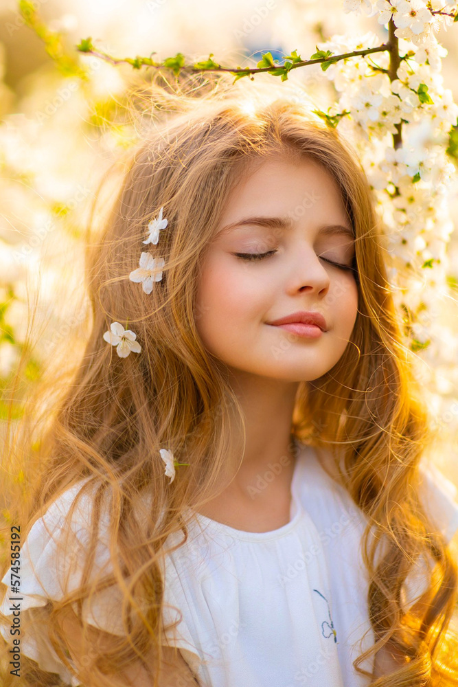 Fototapeta premium Portrait of beautiful young blonde curly girl with blue eyes posing on spring nature with white blooming trees.Sunny positive colorful photo with amazing teenage model. Light in hair. 
