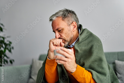 Obraz na płótnie Allergic sick senior man coughing with a sore throat, holding a cup of tea